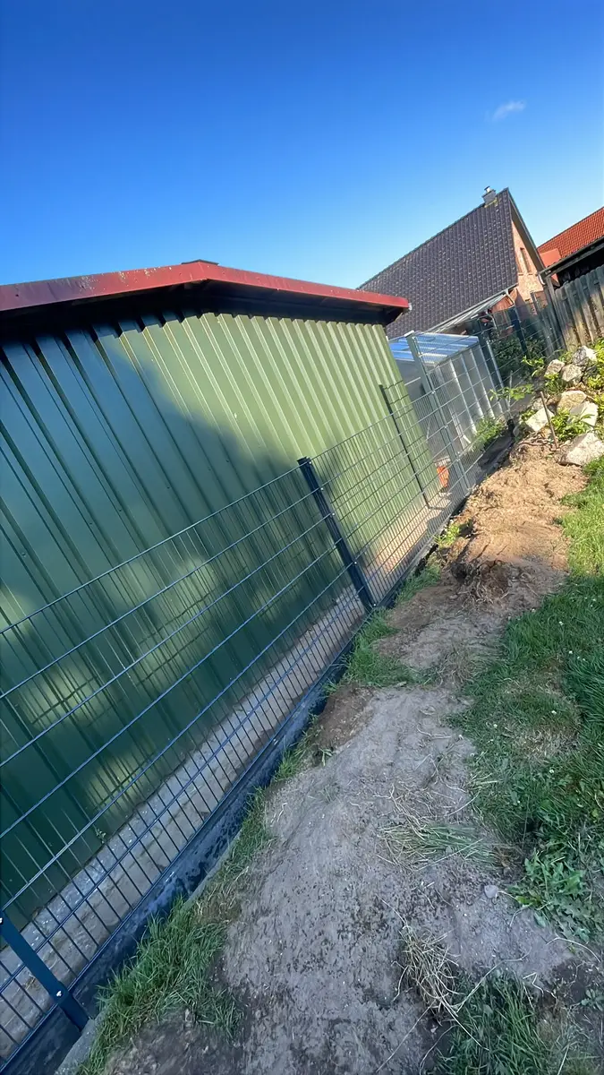 Metallzaun am Schuppen mit frisch verfüllter Erde